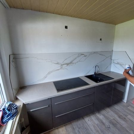 Moderne Küche mit hochglänzend polierten Schränken und einer hellgrauen Keramikarbeitsplatte.